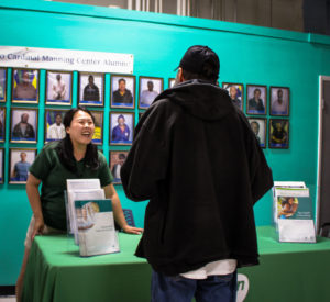 A woman behind a table smiles at a man across from her. The table has brochures and resources for the unhoused community