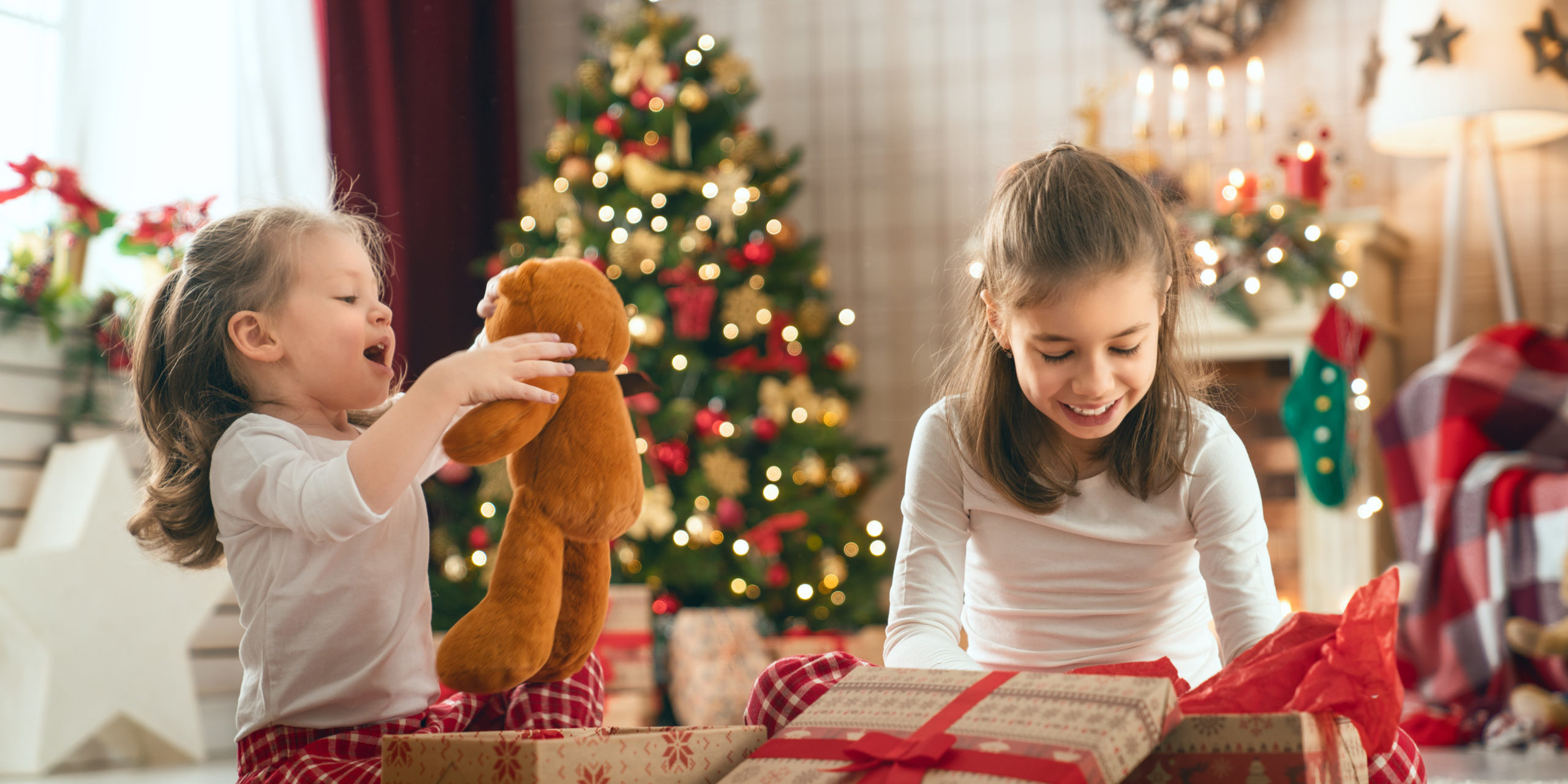 Girls Opening Christmas Gifts Merry Christmas and Happy Holidays! Cheerful cute childrens girls opening gifts. Kids wearing pajamas having fun near tree in the morning. Loving family with presents in room.