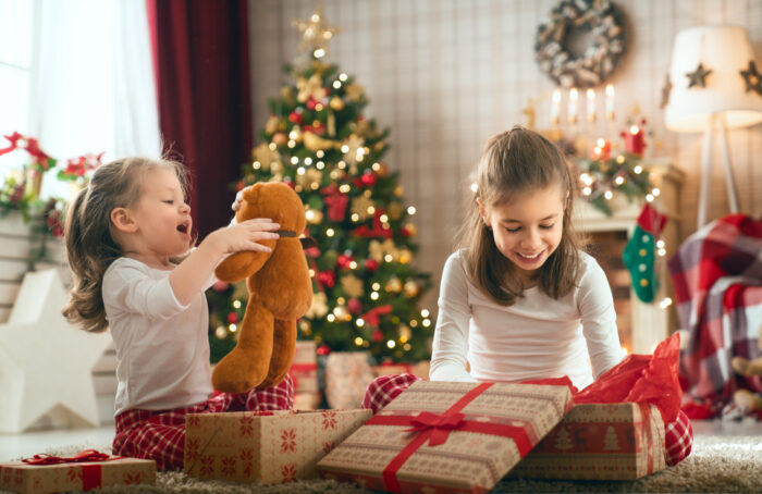 Girls Opening Christmas Gifts Merry Christmas and Happy Holidays! Cheerful cute childrens girls opening gifts. Kids wearing pajamas having fun near tree in the morning. Loving family with presents in room.