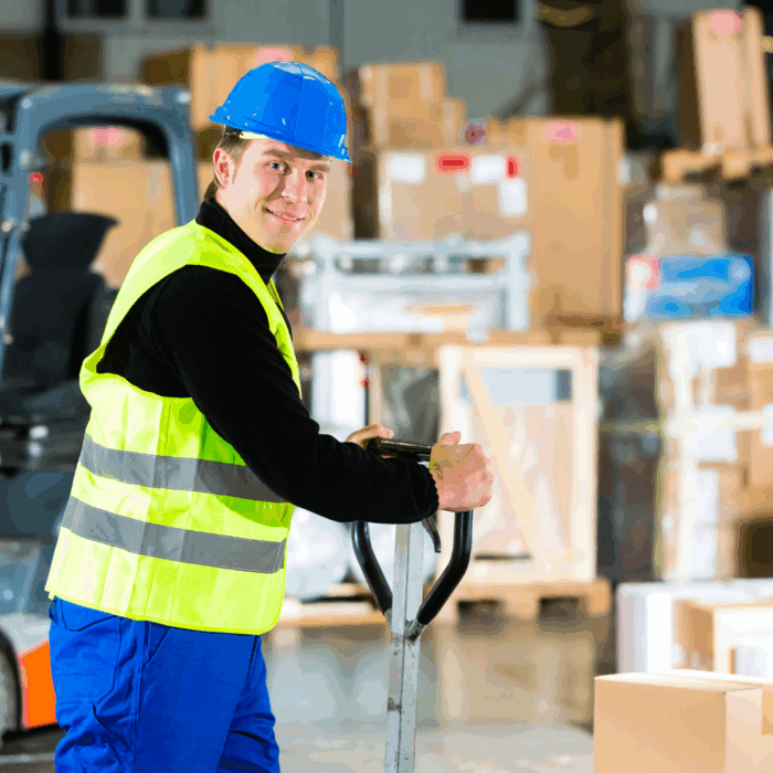 Merchandise handler smiles at camera in front of stacks of boxes. A forklift is beside him