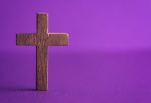 Wooden cross on a purple background. What are you giving up for Lent?