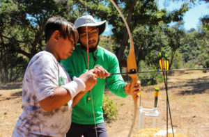 Camp counselor teaches a camper how to hold a bow and arrow.