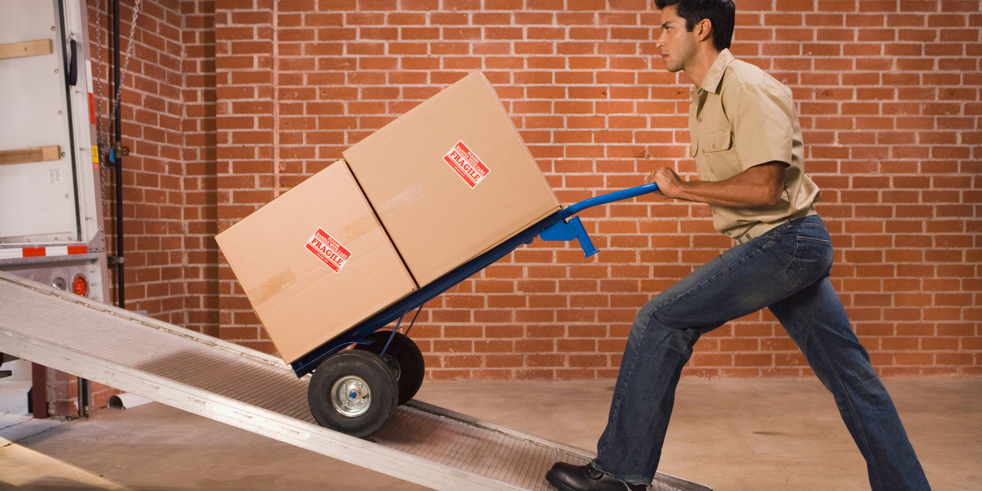 Man uses a dolly to load boxes into a large truck.