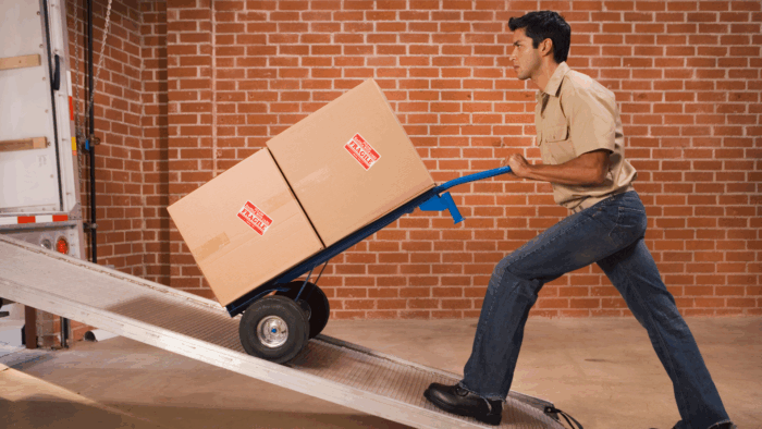 Untitled design (4) Man uses a dolly to load boxes into a large truck.