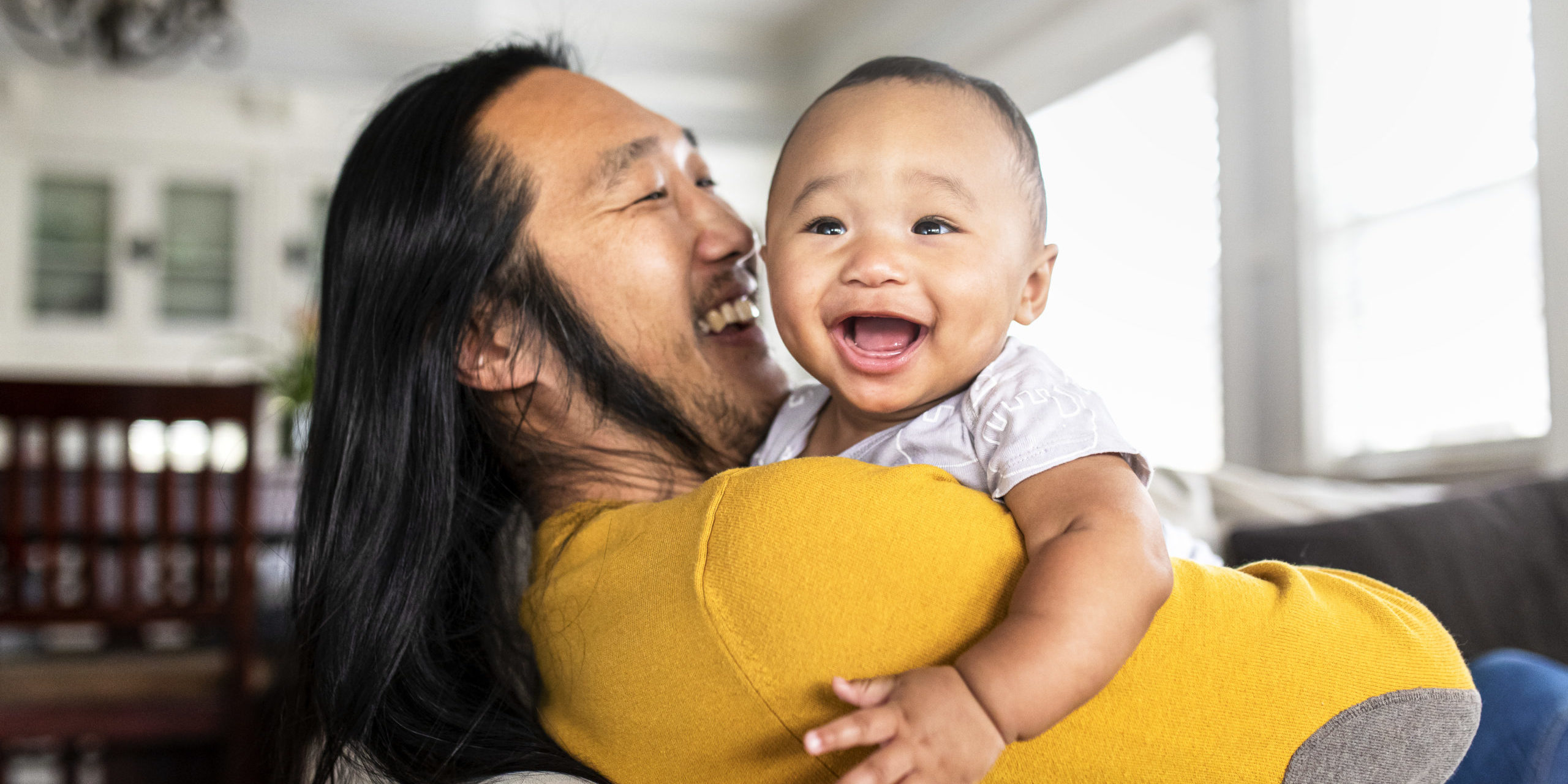 Asian American father hugging his little son A smiling Asian father with long hair holds his laughing baby.