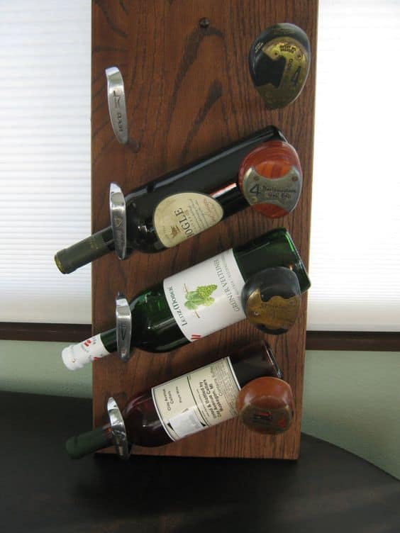 A hommeade wine rack made from a slab of wood and the heads of old golf clubs. Wine bottles hang from the gold clubs.