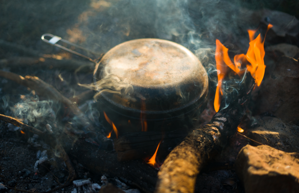 A pan steams in a lit campfire.