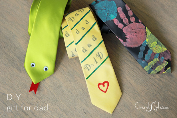 Three neck ties lay on the ground. Each tie is decorated differently. One is dressed to look like a snake. Another says "Dad" multiple times. Another has children's handprints.